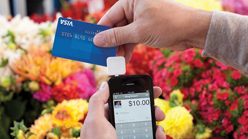 At a flower shop, a merchant swipes a Visa card through a Square reader attached to a phone.