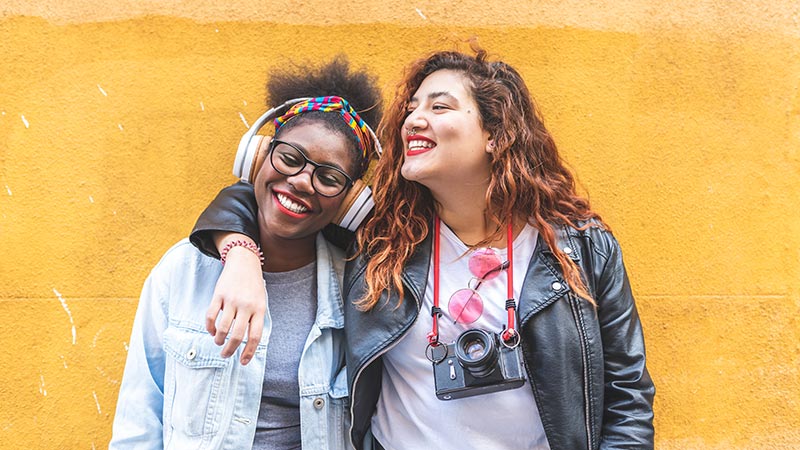 Two Teenage Latin Girls Standing Together Over a Yellow Wall.